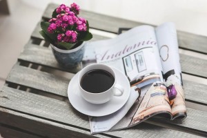 Esta es una imagen de una revista sobre una mesa, junto a un café y unas flores.